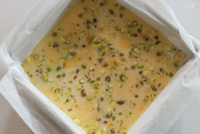 Unbaked lemon pistachio bars in a square baking dish lined with parchment paper.