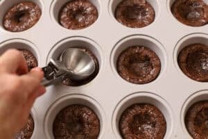 A scoop pressing brownies into a muffin pan.