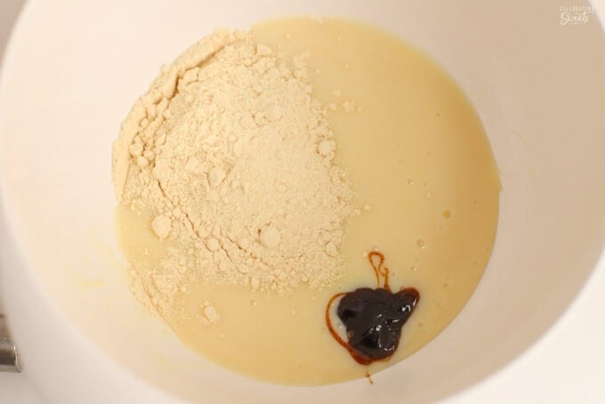Sweetened condensed milk, malt powder, and vanilla bean paste in a large white bowl.