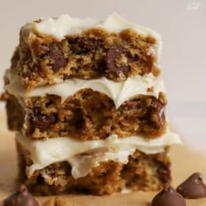 Stack of three oatmeal chocolate chip bars topped with white frosting surrounded by four large chocolate chips.