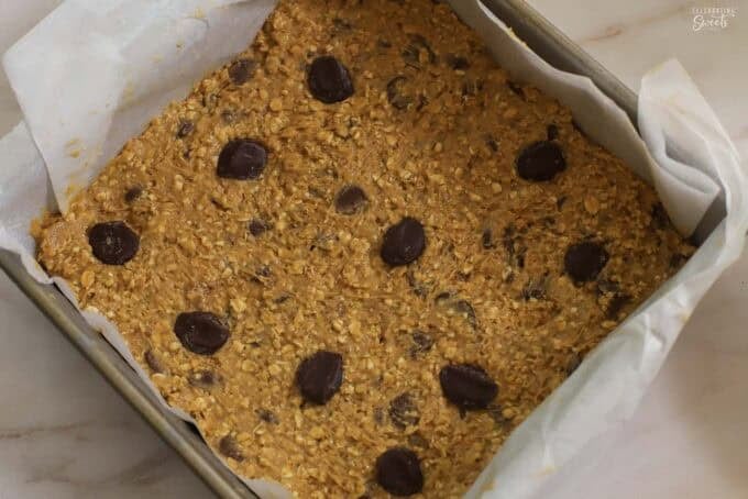 Unbaked oatmeal chocolate chip cookie dough in a square pan topped with chocolate chips.