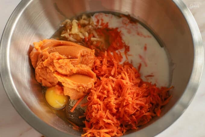 Ingredients for pumpkin carrot cake in a metal bowl: pumpkin, eggs, carrots, milk, sugar, vanilla.