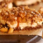 An apple cheesecake bar topped with caramel sauce on a wooden board.