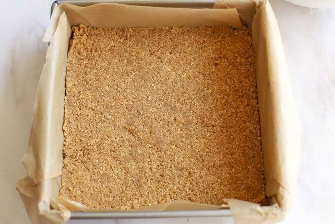 Graham cracker crust in a parchment-lined square pan.