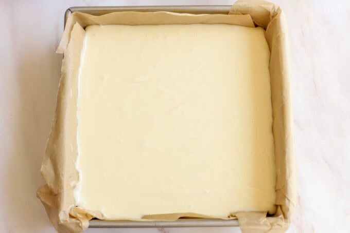 Unbaked cheesecake in a parchment-lined square baking pan.