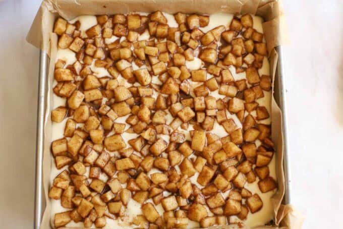 Diced apples on top of cheesecake batter in a square pan.