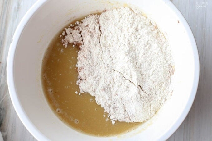 Flour on top of cake batter in a large white bowl.