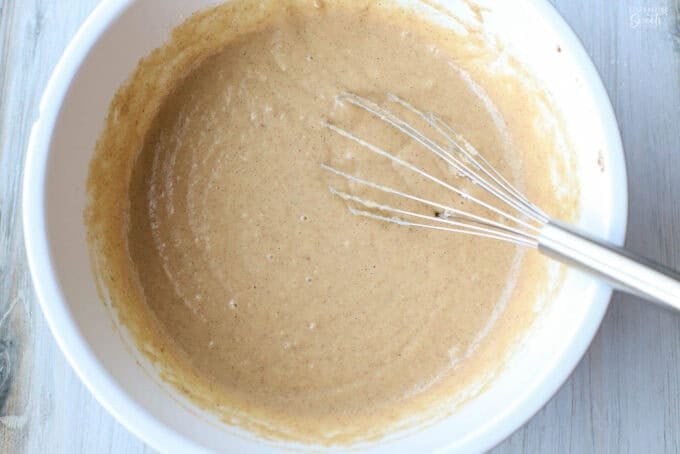 Applesauce cake batter in a white bowl with a whisk in it.