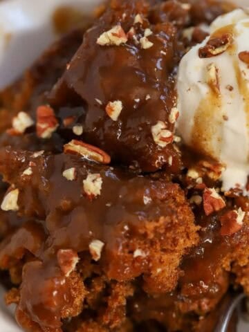 Pumpkin pudding cake in a white bowl topped with a scoop of vanilla ice cream.