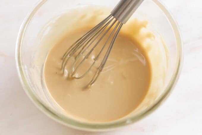Maple icing in a glass bowl with a whisk.