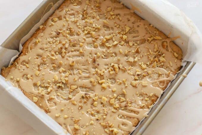 Maple walnut bars in a square pan drizzled with maple icing and topped with chopped walnuts.
