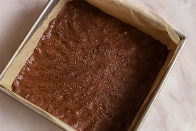 Unbaked chocolate cookie dough in a square metal pan.