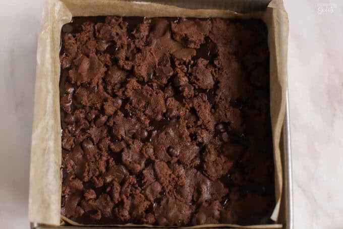 Unbaked chocolate cookie bars in a parchment-lined square pan.