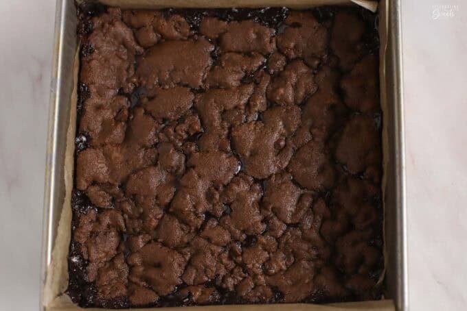 Baked chocolate cookie bars in a parchment-lined square pan.