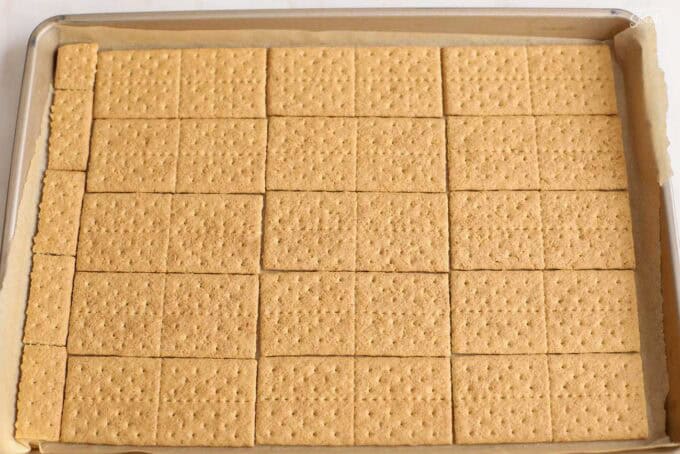 Graham crackers laid out on a parchment-lined baking sheet.