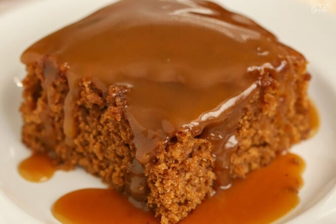 Slice of gingerbread cake on a white plate topped with toffee sauce.
