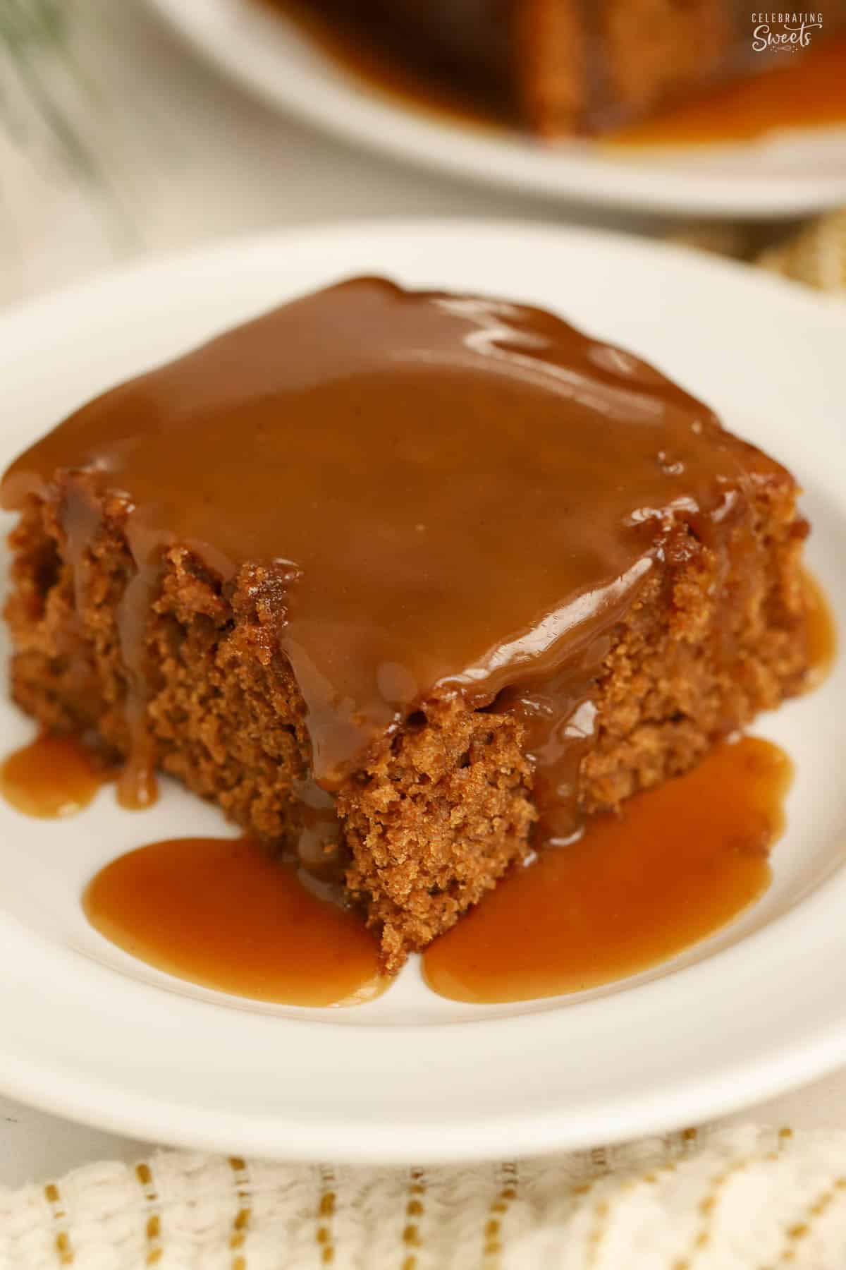 Slice of gingerbread cake on a white plate topped with toffee sauce.