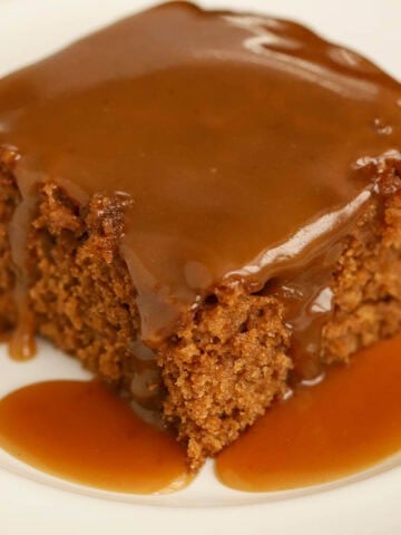 Slice of gingerbread cake on a white plate topped with toffee sauce.