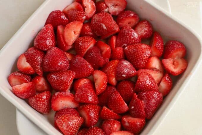 Strawberries tossed in sugar in a white square baking dish.