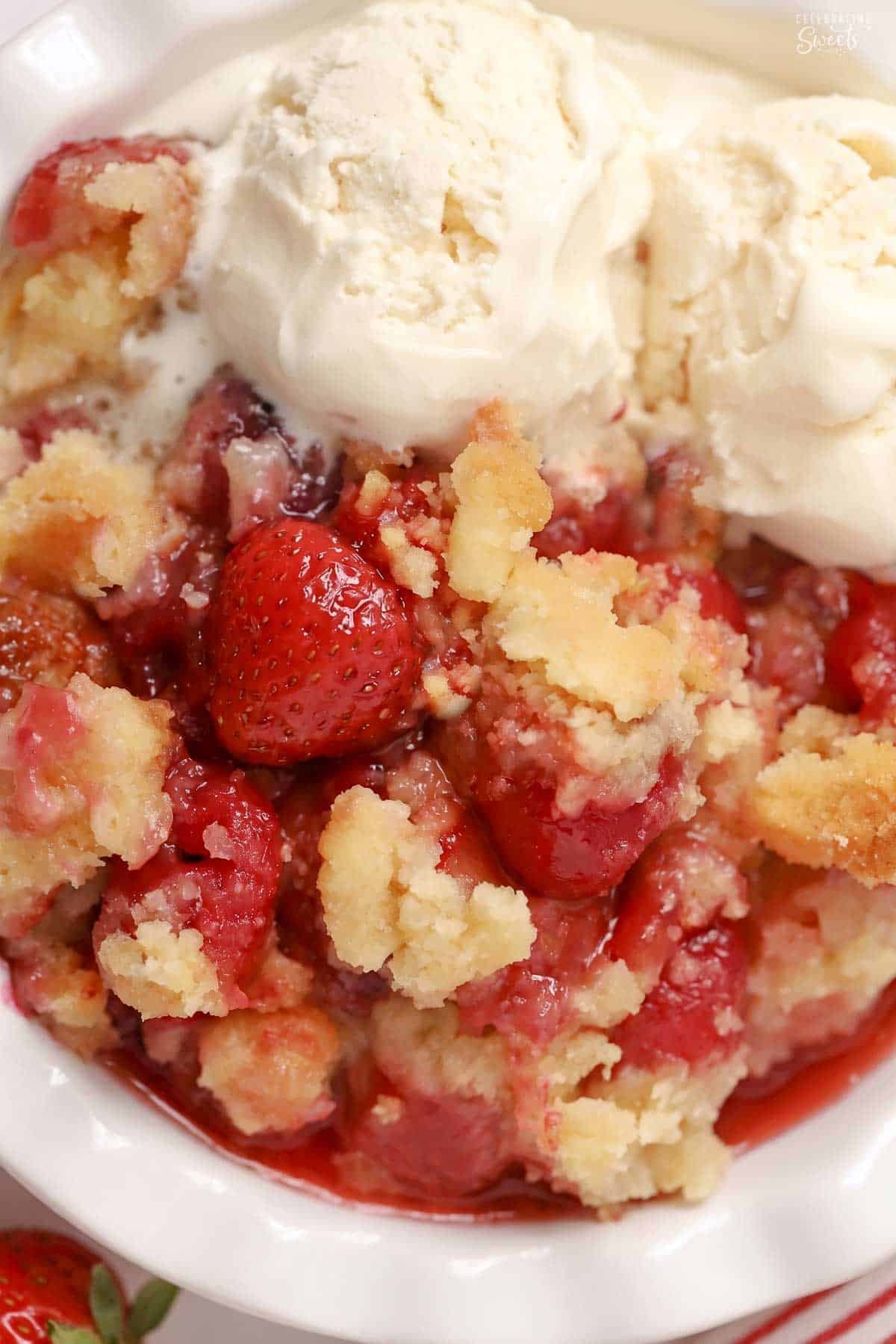 Strawberry cobbler topped with a scoop of vanilla ice cream in a white bowl.