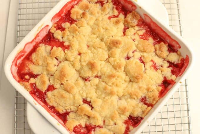 Strawberry cobbler in a white square baking dish set on a wire rack.