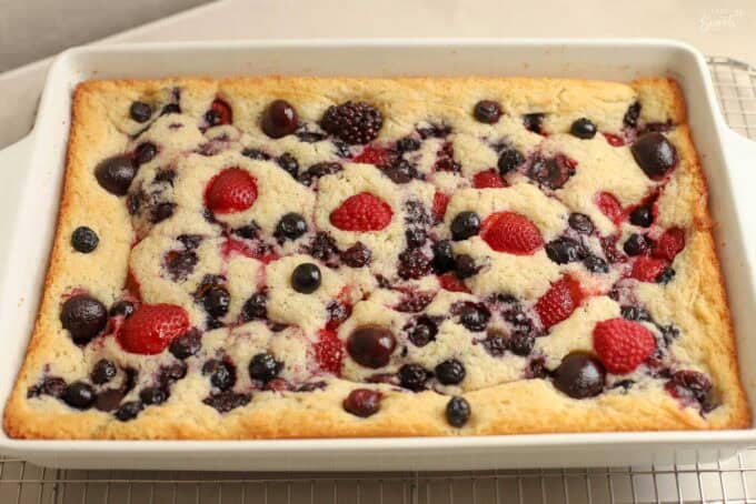 Vanilla spoon cake topped with berries and cherries in a white rectangular baking dish.