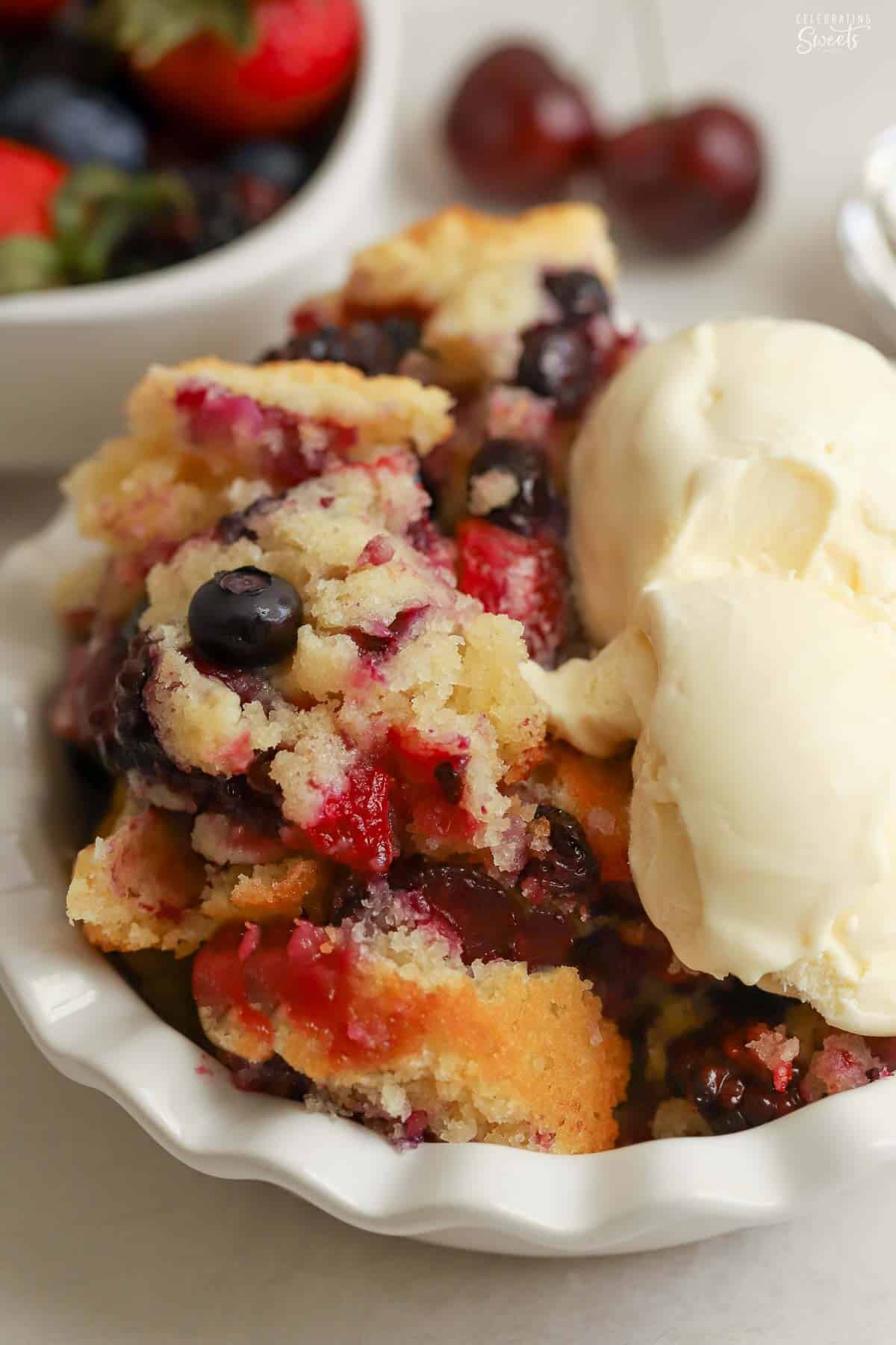 Spoon cake with berries scooped into a white bowl next to a scoop of vanilla ice cream.