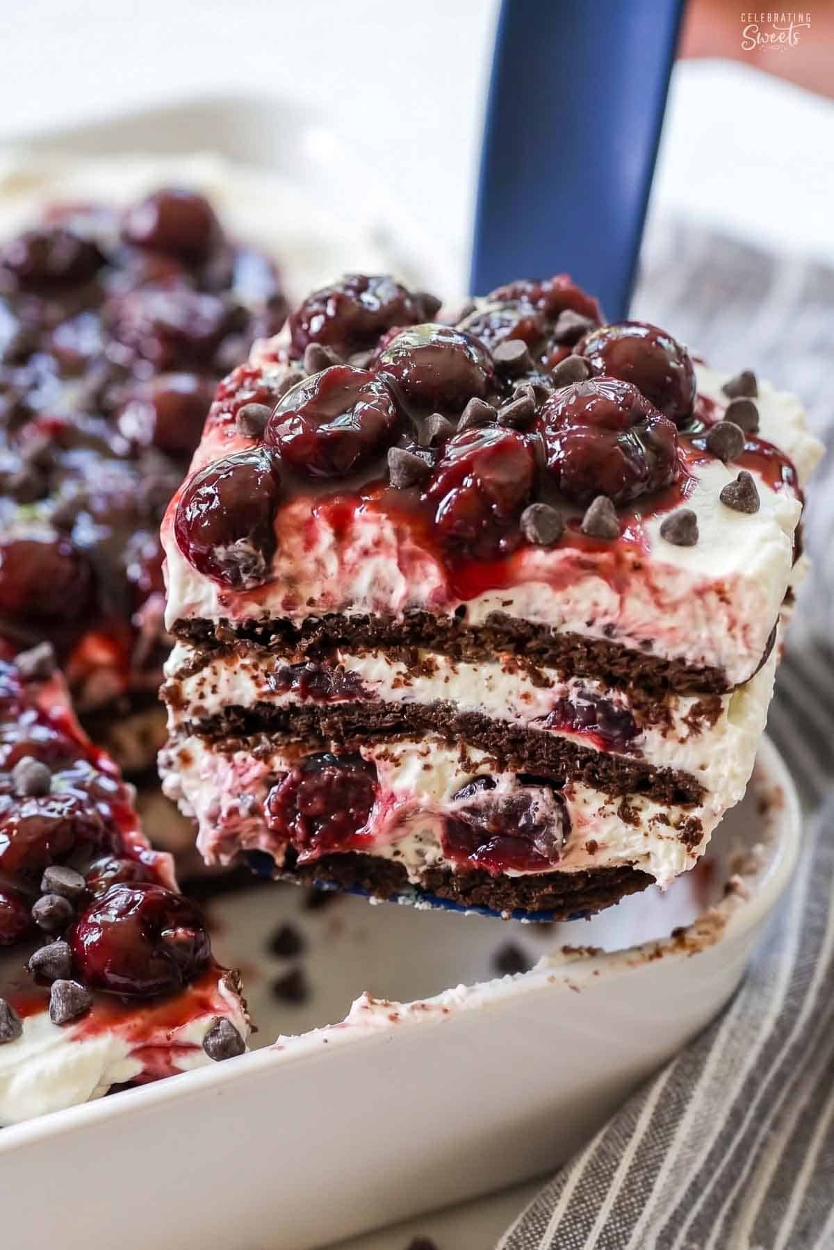 A slice of black forest icebox cake on a blue spatula next to a grey striped napkin.