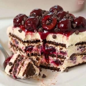 A slice of black forest icebox cake topped with cherries on a white plate.