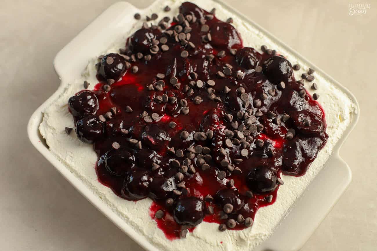 Black forest icebox cake in a square white pan topped with cherries and chocolate chips.