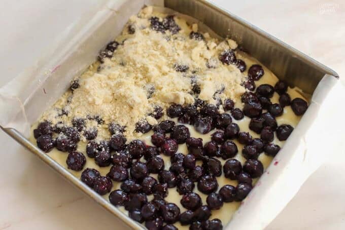 Unbaked lemon blueberry crumb bars in a parchment-lined square pan.
