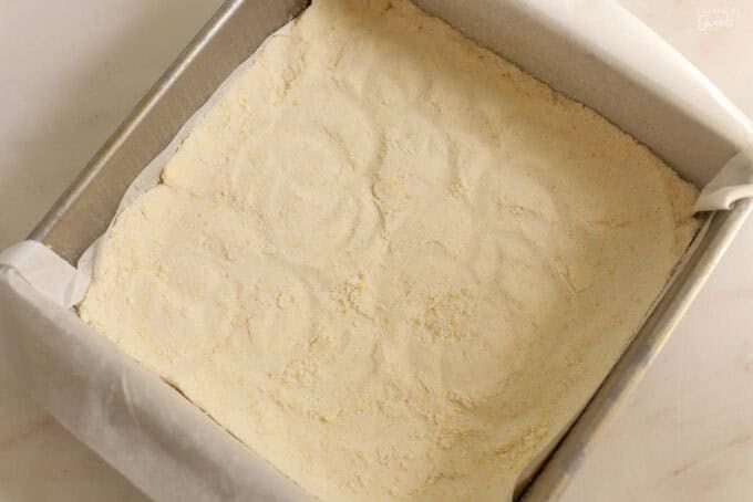 Unbaked lemon shortbread crust in the bottom of a square baking pan.
