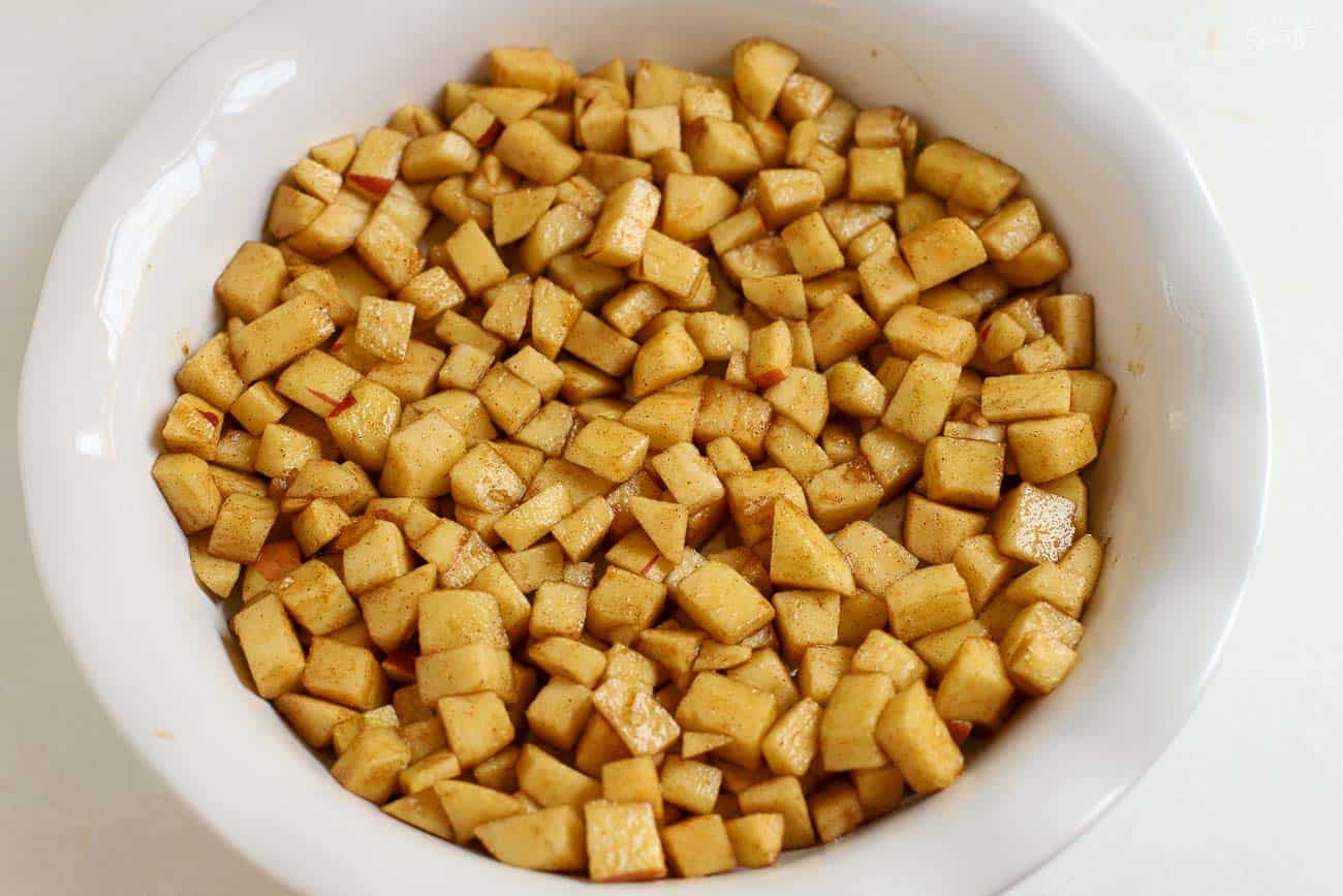 Diced apples tossed in cinnamon sugar in a white round baking dish.